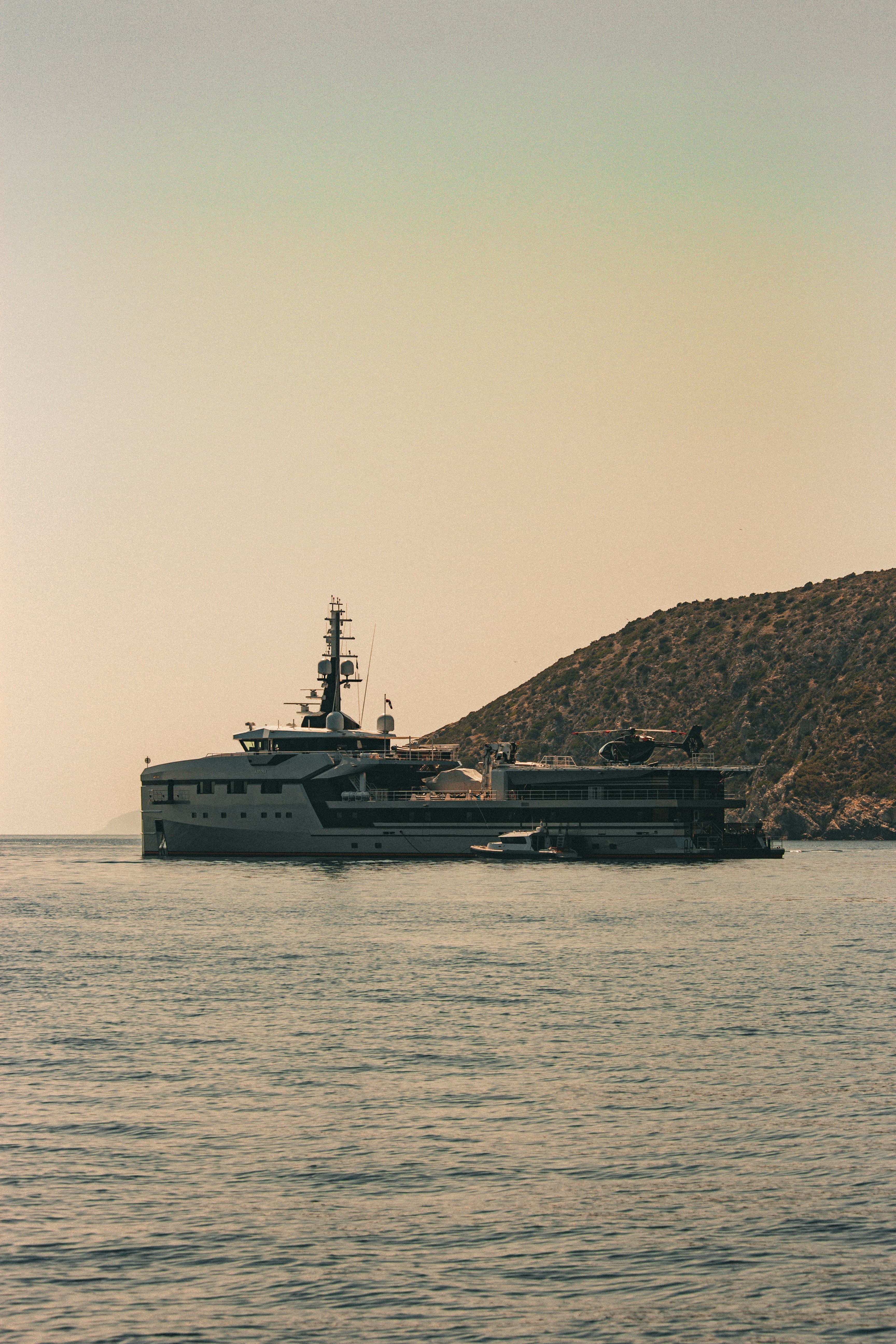 Explorer-style superyacht at sunset against a Mediterranean headland